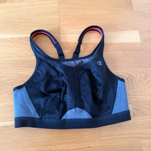 Champion sport-bh svart och grå - Sport-bh från Champion i svart och grått med röda detaljer. Modellen har justerbara axelband, meshpaneler för extra ventilation och hakknäppning bak. Perfekt för träning med max support och snygg atletisk look. Den är inte så stretchig så skulle säga att det mer lutar åt XS-hållet. Den kan vara lite nopprig. 