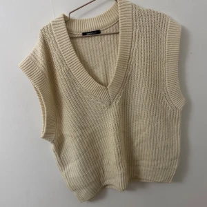 Beige stickad väst från Gina Tricot - Beige stickad väst från Gina Tricot med bred ribbad v-ringning och grovstickad struktur. Modellen är ärmlös och har en avslappnad passform, perfekt att slänga över en skjorta eller t-shirt för en trendig lager-på-lager-look. Den är i storlek L för att jag ville ha den pösig, då jag tycker att det är finare med oversize look just på dessa typer av tröjor. 