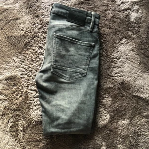 Grå jeans från Jack & Jones, 30/32 - Säljer ett par grå jeans från Jack & Jonesi storlek 30/32. Jeansen har klassisk femficksdesign, raka ben och snygga slitningar för en cool look. Materialet är mjukt denim och färgen är en tvättad grå nyans. Perfekta för dig som gillar stilrena och bekväma jeans.