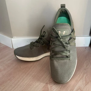 Gröna sneakers från Under Armour - Snygga gröna sneakers från Under Armour med mesh-ovandel och gröna snören. Skorna har en vit och grön sula med logga undertill, samt metallic-detaljer i brons på hälen. Insidan är mintgrön med logotyp. Perfekta för träning eller chill.  Storlek 38 men Lite mindre i storlek använda 2 kortare stunder 
