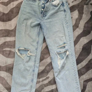 Ljusa ripped jeans - Snygga ljusblå jeans med slitna detaljer och hål på båda benen från H&M DIVIDED. Modellen har hög midja, raka ben och klassisk knappgylf.