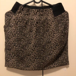 Leopardmönstrad kortkjol med resår - Snygg kortkjol med leopardmönster och bred svart resår i midjan. Kjolen har en beige bas med svarta och bruna fläckar som ger en cool och trendig look. Perfekt för dig som vill sticka ut med ett djurmönster.