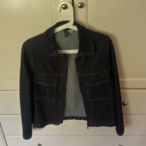 Mörkblå jeansjacka från H&M Divided XS - Snygg mörkblå jeansjacka från H&M Divided i storlek XS. Klassisk modell med två stora bröstfickor, raka sömmar och lång ärm. Perfekt för dig som gillar en enkel och tidlös look. Jackan är i ett robust denimtyg och har en rak passform.