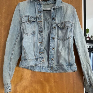 Ljusblå jeansjacka från Hennes, stl 36 - Snygg ljusblå jeansjacka från Hennes collection i klassisk modell med knappar framtill och två bröstfickor med lock. Jackan har långa ärmar och är tillverkad i denim med kontrastsömmar. Perfekt för dig som gillar en tidlös och avslappnad stil.
