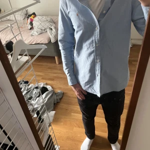 Ljusblå skjorta från Polo Ralph Lauren - Säljer en klassisk ljusblå skjorta från Polo Ralph Lauren med broderad logga på bröstet. Skjortan har lång ärm, knappar framtill och är tillverkad i 100% bomull. Perfekt för dig som gillar stilrena och tidlösa plagg.