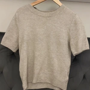 Beige stickad kortärmad tröja - Superfin beige stickad tröja med korta ärmar och rund hals. Tröjan har ribbade muddar vid ärmslut och nederkant, vilket ger en snygg och enkel look. Perfekt att matcha med jeans eller kjol för en chill stil.