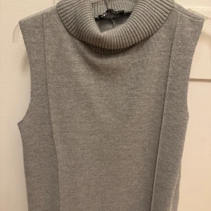 Grå ärmlös polotröja från Zara - Säljer en stilren grå ärmlös polotröja från Zara. Tröjan har en hög, ribbad polokrage och är stickad i mjukt material. (Den är längre än bilden)
