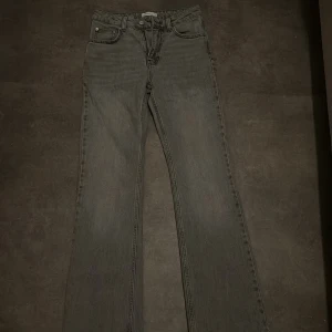 Grå raka jeans med hög midja - Säljer ett par grå jeans med raka ben och hög midja. Klassisk femficksmodell med knapp och dragkedja framtill. Jeansen har en stilren look och är tillverkade i ett mjukt denimtyg som är skönt att bära hela dagen.