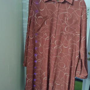 Brun mönstrad skjortklänning By Alba - Snygg brun skjortklänning från By Alba med vita prickiga linjer som mönster. Klänningen har lång ärm, två bröstfickor och knäppning framtill. Perfekt för dig som gillar en avslappnad men ändå stilren look.