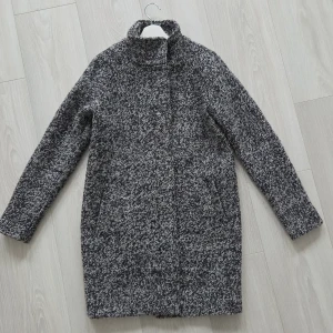 Snygg ullkappa med dragkedja - Säljer en fin stilren ullkappa med hög krage.Jackan har en melerad look i vit,grå och svart.Den är i nyskick då jag knappt har användt den.Längden är 89 cm💕