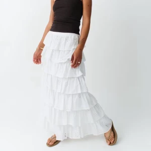 Vit långkjol med volanger - Supersöt vit långkjol med flera lager volanger och broderade detaljer. Kjolen är gjord i bomull och har en luftig, flowy känsla som är perfekt för varma dagar. Helt slutsåld och använd cirka 1 gång. Köpt för 800