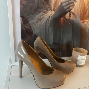 Beige pumps med hög klack - Snygga beige pumps med rund tå och hög klack. Skorna har en glansig finish och plattform framtill som ger extra höjd och stabilitet. Perfekta för dig som vill ha en stilren och elegant look med lite edge.