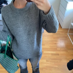 Mörkgrå stickad tröja från Amisu - Mysig mörkgrå stickad tröja från Amisu med rund halsringning och långa ärmar. Tröjan har ribbade muddar vid ärmslut och nederkant, perfekt för kyliga dagar. Enkel och stilren design som passar till allt.