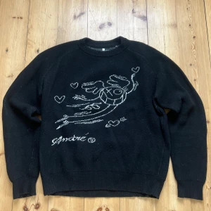 Svart stickad tröja från Soulland - Svart stickad tröja från Soulland med vit broderad illustration på framsidan. Rund halsring muddar. Perfekt för dig som gillar unika prints och streetwear vibes.