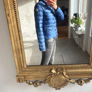 Blå Moncler dunjacka - Snygg blå dunjacka från Moncler med klassisk logga på ärmen. Jackan har quiltad design, dragkedja framtill och två fickor med lock. Perfekt för kyliga dagar och ger en clean, sportig look. Den är köpt på nk. Har qr kod skriv för fler bilder💗