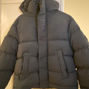 Trapstar mörkgrå pufferjacka - Hjälper min kille att sälja sin trapstar vinter jacka, jackan har inga tecken på slitage och har tagits väl hand om. Jackan har  Trapstar loggan fram och bak samt en badge på ärmen.