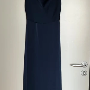 Marinblå långklänning från Vila - Marinblå långklänning från Vila med tunna axelband och lätt draperad urringning. Klänningen har en elegant, slät siluett och är tillverkad i ett mjukt, följsamt materia. Aldrig använd.