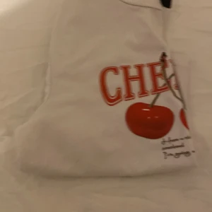 Vit t-shirt med körsbärstryck från SHEIN - Vit t-shirt från SHEIN i storlek S med ett stort körsbärstryck och texten 'CHERRY' i rött framtill. Klassisk rund halsringning och korta ärmar. Perfekt för dig som gillar fruktiga prints och en chill vibe.