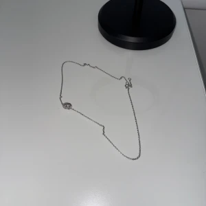 Silverfärgat halsband  - Stilrent halsband i silverfärg med en tunn kedja och ett hänge i form av två tvinnade cirklar, varav en är dekorerad med små glittrande stenar. Perfekt för dig som gillar minimalistiska smycken med en touch av elegans.