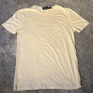 Beige t-shirt från Polo Ralph Lauren - Snygg beige t-shirt från Polo Ralph Lauren med klassisk passform. T-shirten har rund hals, korta ärmar och en bröstficka med broderad logga. Tillverkad i mjuk bomull som känns skön mot huden. S/M