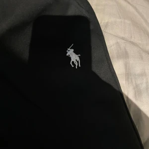 Svart sett från Polo Ralph Lauren - Svarta byxor från Polo Ralph Lauren med klassisk broderad logga i vitt på ena benet samt en matchade kofta till. Perfekta för en chill och stilren look. Storlek S i båda, aldrig använts 