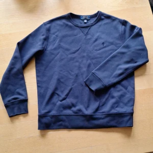 Mörkblå sweatshirt från Polo Ralph Lauren - En klassisk mörkblå sweatshirt från Polo Ralph Lauren med rund hals och diskret broderad logga på bröstet. Tröjan har långa ärmar, ribbade muddar och är gjord i mjuk bomull. Perfekt för en chill och stilren look.