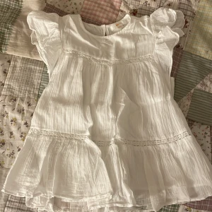 Vit volang blus från Gina Tricot - Supersöt vit volang blus från Gina Tricot i 100% bomull. Blusen har volangdetaljer, korta ärmar och fina spetsinslag. Perfekt till sommaren.