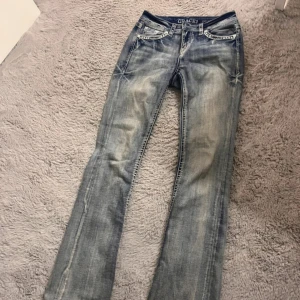 Grace in LA bootcut jeans med broderi - Snygga ljusblå bootcut jeans från Grace in LA med slitningar och broderade detaljer på bakfickorna. Jeansen har klassisk femficksdesign, dekorativa sömmar och är tillverkade i jeansmaterial. Perfekta för dig som gillar en lite western-inspirerad look.