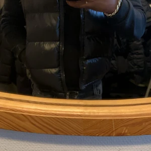 Svart dunväst från Moncler - Svart, glansig dunväst från Moncler med klassisk logga på bröstet. Västen har quiltad design och dragkedja framtill. Materialet är polyester och dun, vilket gör den både lätt och varm. Perfekt för lager-på-lager och har en clean, modern look.