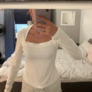 Tröja - Säljer en stilren vit långärmad tröja med snygg fyrkantig ringning. Tröjan är figurnära och har en clean look som passar perfekt till jeans eller kjol. Materialet känns mjukt och stretchigt, vilket gör den riktigt bekväm att bära.