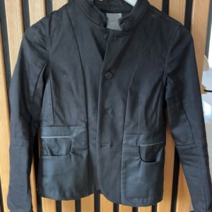 Svart kavaj - Stilren svart kavaj med ståkrage och knäppning framtill. 