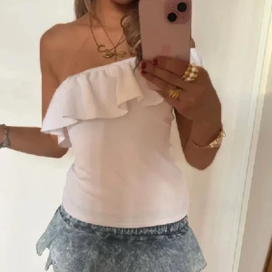Vit offshoulder topp med volang - Supersöt vit offshoulder topp med bred volang över bysten. Sitter tight och är ärmlös, perfekt till sommarens alla tillfällen. Tunn och mjuk bomullskänsla, enkel att matcha med både kjol och jeans. Lånade bilder från tjejen jag köpte från så det är exakt samma tröja!