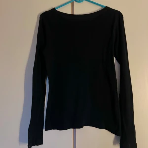 Svart långärmad topp - En basic svart långärmad topp i enkel och stilren design. Toppen har rund halsringning och är tillverkad i mjukt bomullsmaterial, perfekt att matcha med jeans eller kjol för en clean look.