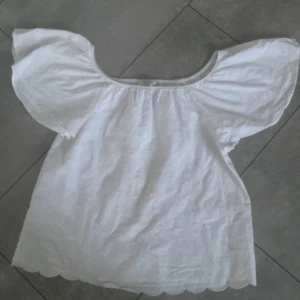 Vit blus med volangärm från LCW Girls - Söt vit blus från LCW Girls med breda volangärmar och rund halsringning. Blusen har broderade detaljer i tyget och en vågig kant längst ner. Perfekt för en fräsch och somrig look. Xxs/152!