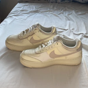 Nike Air Force 1 - Säljer ett par Nike Air Force 1 sneakers i en beige och vit färgkombination. Använda några gånger så finns lite skavanker och fläckar men är generellt i bra skick! Har stått i hallen i några år så är lite dammiga inuti 😅🤭