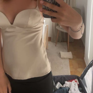 Champagnefärgad satin topp  - Säljer denna snygga topp i champagnefärgad satin med formade kupor och smala axelband, eftersom den är lite för stor för mig i kuporna och inte har kommit till användning. Har använt denna topp en gång och den är i mycket bra skick! Storlek xs 