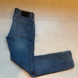 Blå jeans neuw - Snygga blå jeans med klassisk femficksdesign och rak passform. Jeansen har en mörkblå tvätt med lätt slitning och svart patch bak i midjan. Perfekta för en avslappnad och stilren look.