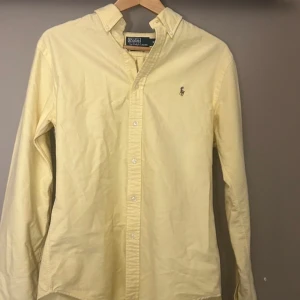 Ralph Lauren skjorta - Gul skjorta från Polo Ralph Lauren i slim fit med klassisk button down-krage och broderad logga på bröstet. Skjortan är långärmad och har knäppning framtill. Perfekt för dig som gillar stilrena och fräscha plagg. Ny pris 1795kr.