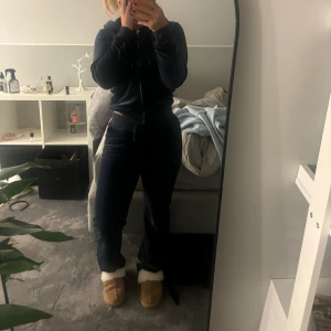 Mörkblå velourbyxor Juicy Couture XS - Mörkblå mjukisbyxor från Juicy Couture i velour med dragsko i midjan och fickor bak med knappar. Klassisk juicy-stil, perfekta för en chill och trendig look. Säljes i storlek XS på tröjan och xxs på byxorna 