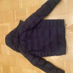 Svart pufferjacka från G-Star RAW - Säljer en svart pufferjacka från G-Star RAW med huva och dragkedja. Jackan har en quiltad look och tydliga loggpatchar på ärmen och nedtill. Perfekt för kalla dagar och har en modern, stilren design.