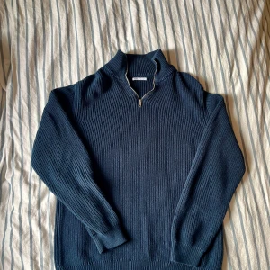 Marinblå stickad half zip från Zara - Säljer en marinblå stickad tröja från Zara med ribbad struktur och half zip-dragkedja vid halsen. Tröjan har lång ärm och hög krage, perfekt för lager-på-lager under kyliga dagar.