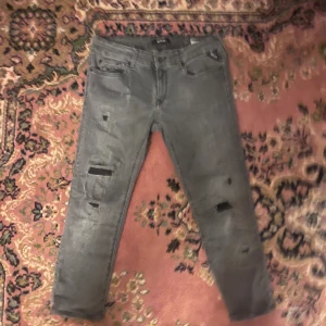 Grå slitna jeans från Replay, strl 29/30 - Säljer ett par grå jeans från Replay i modellen LUZ. Jeansen har flera slitningar och hål på benen för en riktigt edgy look. Klassisk femficksmodell med dragkedjegylf och smal passform. Perfekta för dig som gillar streetstyle. Midja 36cm längd 76cm (42)