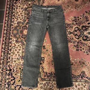 Grå Lee West jeans slim fit 31/32  - Snygga grå jeans från Lee med klassisk femficksdesign och raka ben. Jeansen har en tvättad look med ljusa slitningar och Lee-logga på bakfickan och linningen. Tillverkade i slitstarkt denimtyg som ger en cool och avslappnad vibe. Midja 38cm längd 104cm (58)