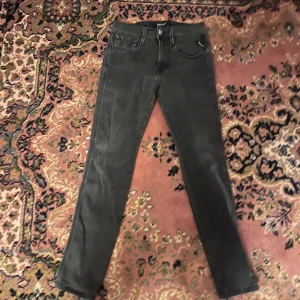 Replay Anbass mörkgrå slim jeans 27/32  - Svarta Replay Anbass jeans med skinny passform och klassisk femficksdesign. Jeansen har diskreta slitningar och snygga detaljer vid fickorna. Tillverkade i stretchigt denim för en bekväm känsla och snygg siluett. Midja 32cm längd 90cm (48) 