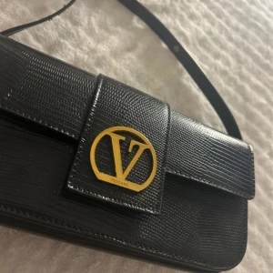 Vezzano bag - Elegant Vezzano Crossbody Bag - Black Faux Leather with Lizard Effect Original price: approx. 1300 SEK | Selling for: 400SEK Stylish and versatile bag from Vezzano, featuring a structured silhouette and gold-tone hardware. The textured faux leather gives a luxurious lizard-skin effect - perfect for everyday use or special occasions. Coming from a Scandinavian brand that takes inspiration to Italian bags Adjustable strap • Magnetic flap closure with bold V-logo Gold hardware