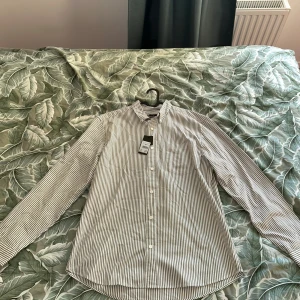 Randig skjorta från Cubus i bomull - Snygg skjorta från Cubus med smala svarta och vita ränder, klassisk krage och bröstficka. Långärmad modell i mjuk bomull med knäppning framtill. Perfekt för en clean och stilren look. Hör av dig vid minsta lilla fråga:)