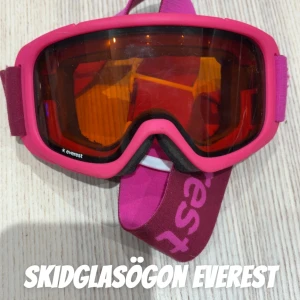 Rosa skidglasögon från Everest - Snygga skidglasögon från Everest i rosa med orange tonade linser. Bred elastisk rem med logga och bekväm passform. Perfekta för vinterns äventyr i backen. Passar 7-11år