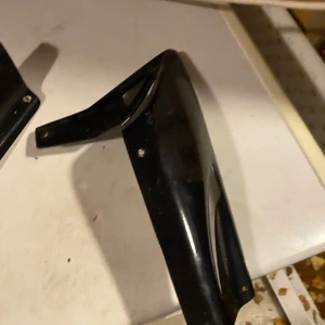 Bcd underkåpa - Två svarta plastdetaljer, troligen kåpor eller skydd för fordon eller maskin. De har flera monteringshål och en sportig design. Ytan visar mindre repor och slitage, men inga större skador syns. Perfekt för dig som behöver reservdelar eller vill byta ut slitna kåpor.