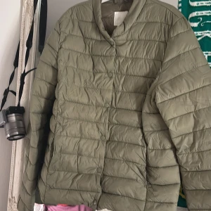 Olivgrön quiltad pufferjacka H&M - Olivgrön pufferjacka från H&M i storlek 36. Jackan är quiltad med horisontella sömmar, har tryckknappar framtill och en enkel, stilren krage. Perfekt för kyligare dagar och lätt att matcha med olika outfits.