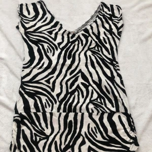 Zebramönstrad kort klänning - Snygg kort klänning med zebramönster i svart och vitt. Klänningen har v-ringning och är ärmlös, perfekt för dig som vill sticka ut med ett djurmönster. Materialet känns mjukt och följsamt mot kroppen.